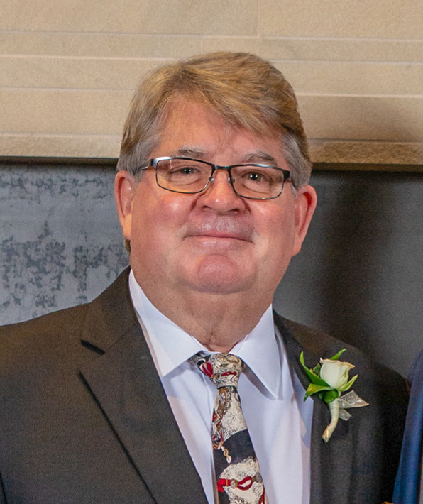 Tom Fitzerald Sr. in a suit that is grey and a red white and blue tie. He is wearing glasses and has grey hair.